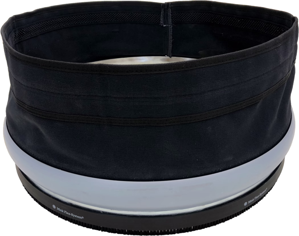 PALLMANN_dummy_SPIDER DUST SEALING SLEEVE_msl_2018-04 Gros plan du bord supérieur et de l'ouverture d'un contenant cylindrique en tissu noir ou d'un chapeau. La photo montre une ouverture circulaire intérieure avec une doublure noire, des coutures renforcées visibles et plusieurs bandes horizontales en tissu à l'extérieur. Près du bord inférieur se trouvent deux larges anneaux en plastique gris clair et une base en caoutchouc noir striée avec de petites dents et un texte imprimé partiellement visible 'Mink Flex-System®'. Le tissu présente un tissage grossier et une finition mate; l'objet paraît structuré mais souple. L'éclairage est uniforme et l'arrière-plan est blanc.
